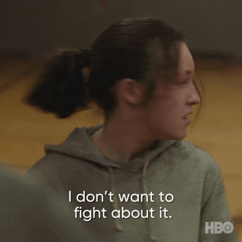 The image shows a woman with long hair wearing a gray hoodie, looking at something off-camera while reading text that says "I don't want to fight about it." The background of the image appears to be a basketball court or gym floor, suggesting an athletic setting.