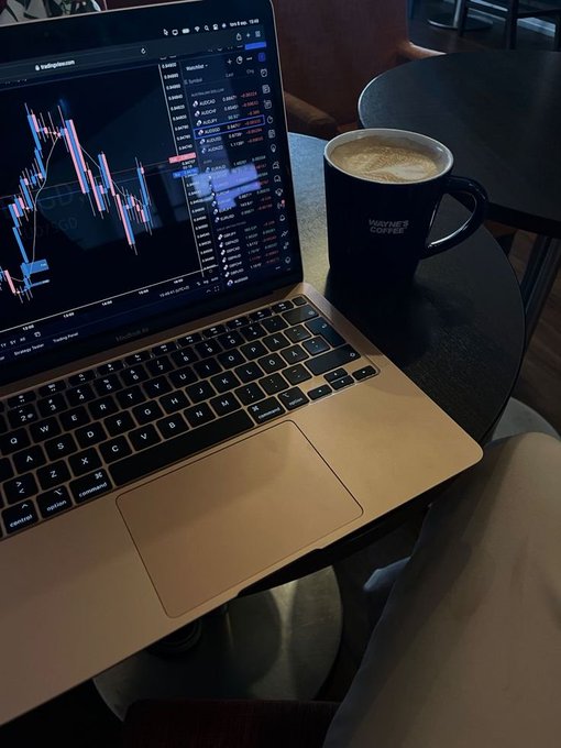 A MacBook laptop displaying a TradingView cryptocurrency chart sits on a dark table next to a 'Wayne's Coffee' mug containing a latte.