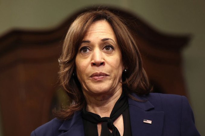 A woman with shoulder-length brown hair, wearing a navy blue blazer with a small American flag pin and a black scarf, looks upward with a serious expression in what appears to be an official setting. The serious demeanor of the figure in the image may visually reinforce the post's cautionary tone about potential market downturns and Bitcoin's cycle ending earlier than expected.