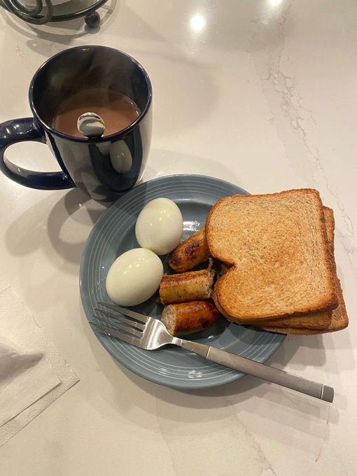 A hearty breakfast of two hard-boiled eggs, breakfast sausage links, and toast on a blue plate, paired with a steaming hot cup of coffee in a dark blue mug, sits on a marble countertop as a perfect fuel-up before sharing crypto wallet details.