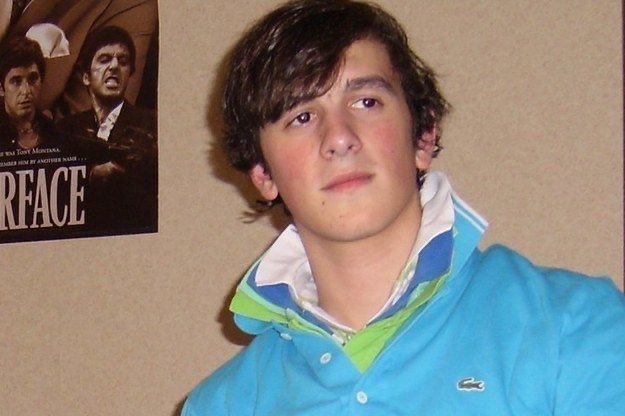 A young man wearing a turquoise Lacoste hoodie poses in front of a Scarface movie poster.