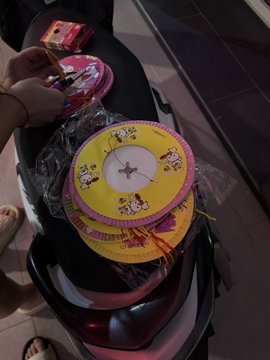 A person holds a yellow round clock featuring Minnie Mouse still in its plastic packaging, with another similar clock visible on a black scooter seat in the background.