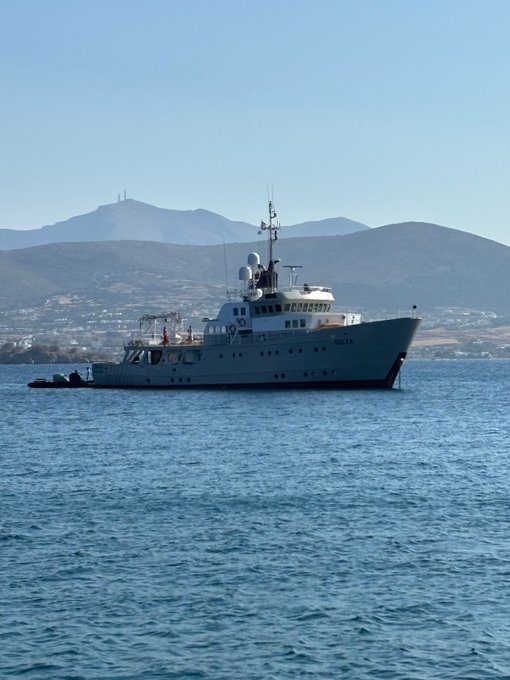 A white ship labeled 'U.S. COAST GUARD' and 'MELLON' floats on blue water with mountains visible in the background.