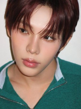 A close-up portrait of a young man with reddish-brown hair wearing a green zip-up sweater, gazing softly at the camera.