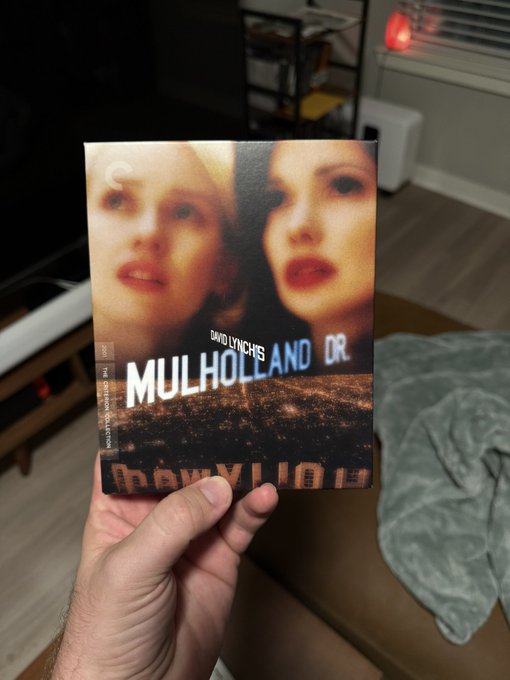 A hand holding up the Criterion Collection Blu-ray of David Lynch's "Mulholland Dr." in a living room setting.