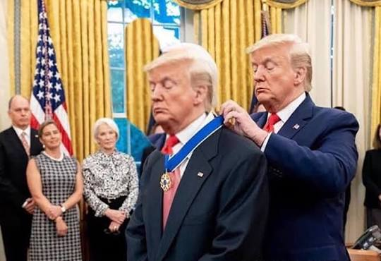 Photo of two men who look like Donald Trump in the Oval Office, with one placing a medal around the other's neck, while other officials including a woman in a black and white checkered dress observe in the background.
