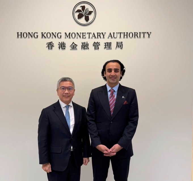 Two men in business suits posing for a photo in front of a wall displaying the Hong Kong Monetary Authority logo and name in both English and Chinese.