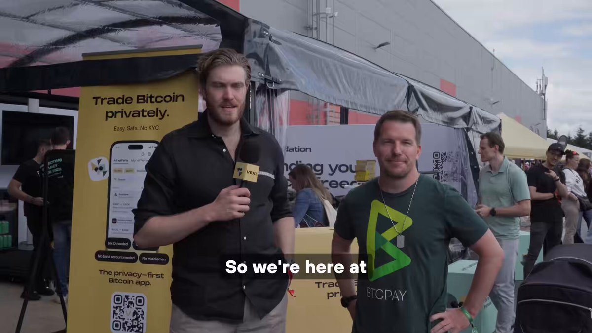 The image features two men standing next to each other, both wearing t-shirts with a green "B" logo. They are posing for a picture together, likely at an event or gathering related to Bitcoin. The background of the photo shows a crowd of people and tents, suggesting that this could be a convention or festival focused on cryptocurrency. The post includes text about Bitcoin and private trading, which is relevant to the image's context.