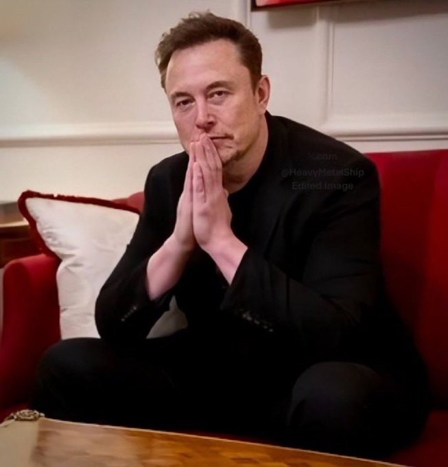 An edited image of Elon Musk sitting cross-legged on a red couch with his hands pressed together in a prayer-like gesture, with faint watermark text '@HeavyMetalShip Edited Image'.