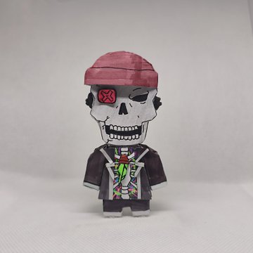 A papercraft figure of a skull character with a pink bandana, an X over one eye, and a colorful jacket stands against a plain background.