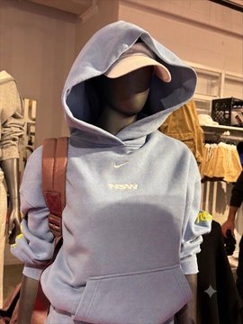A light blue Nike hoodie with a small white swoosh logo is displayed on a mannequin in a clothing store. The user appears to be asking Gemini to help identify or describe the hoodie.