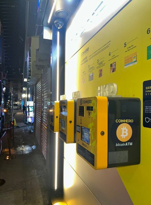 The image shows a row of yellow ATMs, each displaying a Bitcoin logo. The ATMs are located outside at night, with a building visible behind them. A sign next to one of the ATMs reads "Good morning CT. Crypto is growing, BTC ATM". This suggests that there might be an interest in cryptocurrency and digital currency among the people using these ATMs.