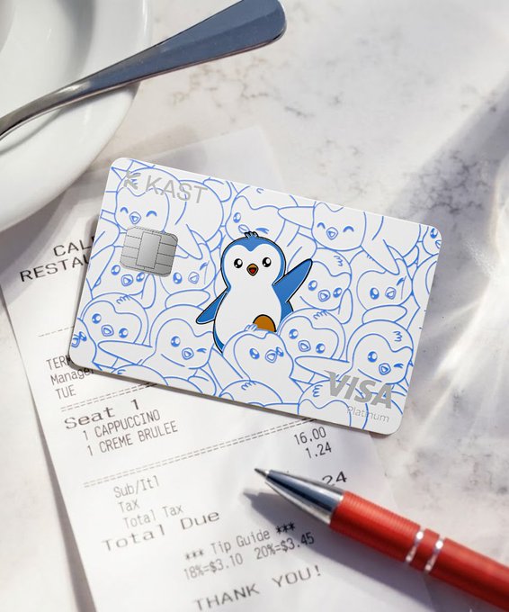 A KAST Visa platinum card with blue penguin designs resting on a restaurant receipt, next to a cup of coffee and a red pen.