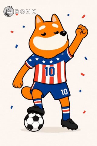 ikura, a Shiba Inu dog, dances with a soccer ball on his hind legs, wearing an American flag-themed jersey and blue shorts against a white background.