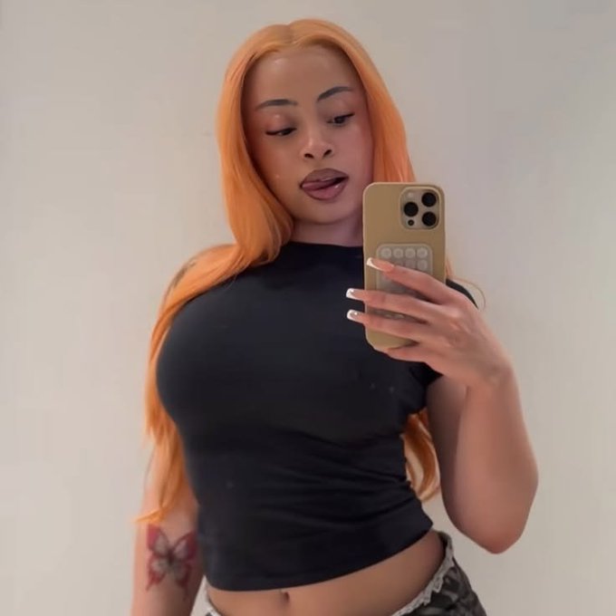 A woman with long orange hair takes a mirror selfie wearing a fitted black short-sleeve crop top, displaying a phone with a tan/gold case. The caption "this or 1 $SOL?" uses her confident appearance as a humorous comparison, playfully suggesting she could be valued at or worth choosing over one Solana (SOL) cryptocurrency.