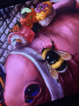 A bumblebee rests on a pink, glossy cupcake or pastry decorated with sunglasses and topped with smaller sweets in a close-up, slightly blurry shot.