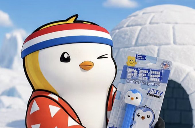 A cute cartoon penguin mascot wearing a red, white, and blue striped headband winks while holding a "Pudgy Penguins Candy & Dispenser" PEZ product in a snowy igloo setting, teasing the upcoming candy collaboration mentioned in the post.