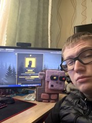 A young boy with glasses proudly displays a pink handheld gaming device in front of a monitor showing the 3D runner game he created for BITFOOTS, showcasing the "KEY:" prompt on screen to highlight the spacebar controls mentioned in his post.