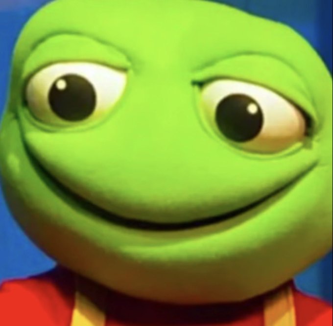 A close-up of a 3D-rendered green frog character with a subtle smile, large eyes, and a red shirt against a blue background.