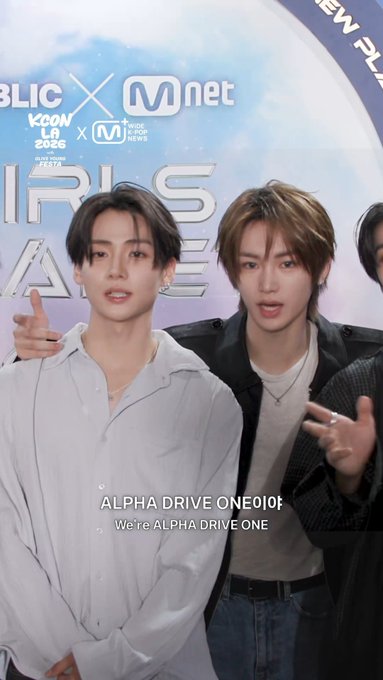 Two young men pose together in front of an "Mnet" and "KCON LA 2025" backdrop, with text on screen reading "ALPHA DRIVE ONE" and "We're ALPHA DRIVE ONE," corresponding to the #ALPHADRIVEONE and #WONXIN hashtags referencing members Sangwon and Anxin.