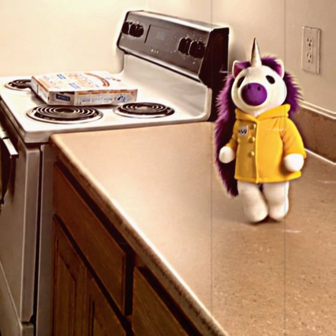 A plush purple and white unicorn toy wearing a yellow raincoat stands on a kitchen counter next to a white stove with an electric range.