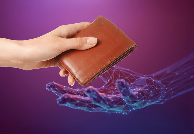 The image features a hand holding an open brown wallet with a few coins inside, set against a purple background. The wallet appears to be made of leather or fabric material. The wallet is being held by a person's hand, which is positioned on the left side of the frame. The wallet has been opened and is now being presented in front of the viewer.