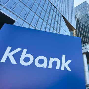 A blue sign displaying the white 'Kbank' logo in front of a modern glass office building.