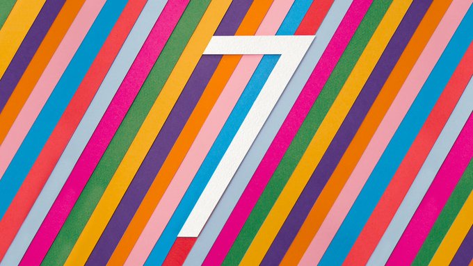The number '7' in white is centered over a background of colorful diagonal stripes in pink, blue, orange, and green.