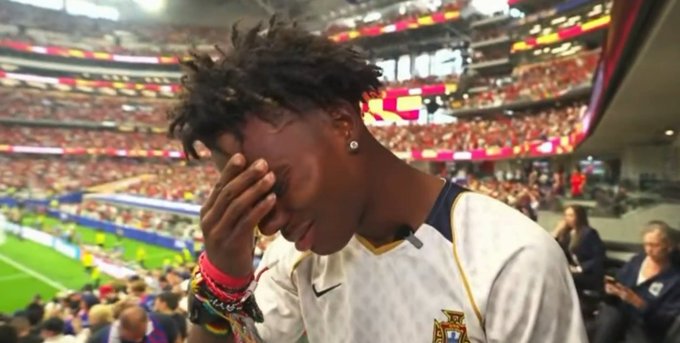 A young man in a Portugal national team jersey covers his face with his hand in apparent frustration or embarrassment at a crowded stadium, fitting the post's joke about an intern at OG (likely a sports betting/sportsbook handle) who has gotten 12 soccer predictions wrong in a row.