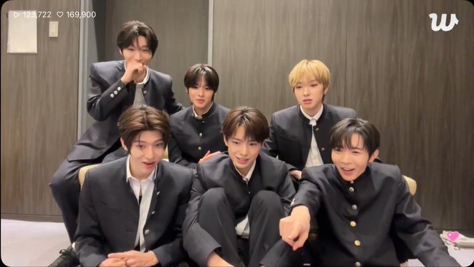 A group of six young men in school uniform-style black jackets pose together, with a 'W' logo in the top right corner and view counts '123,722' and '169,800' in the top left.