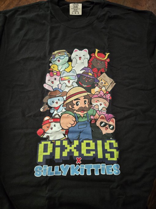 A black t-shirt featuring a colorful graphic design of cartoon characters and cats with the text 'PIXELS X SILLYKITTIES' printed on it.