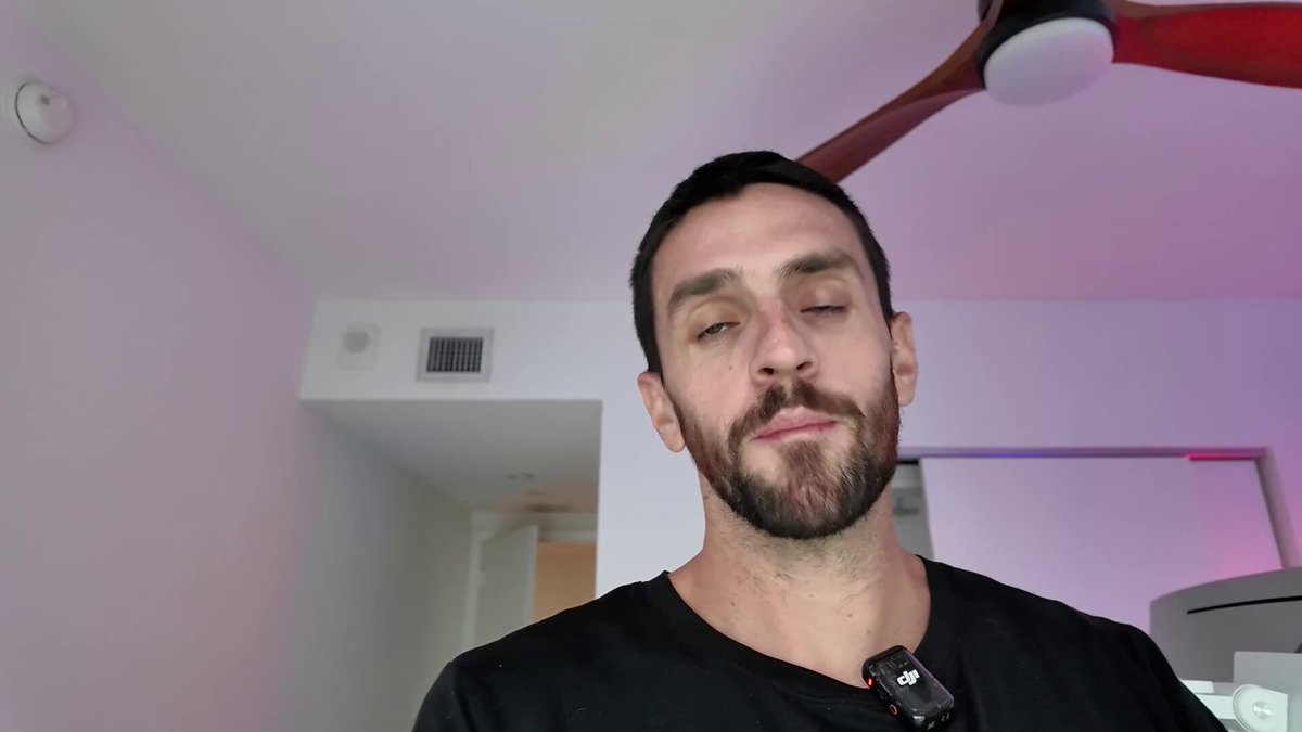 The image features a man with a beard wearing a black shirt who appears to be taking a selfie using his phone's camera. The background of the photo shows a white wall with a ceiling fan, suggesting that they are indoors. There is also an air conditioning unit visible in the room. The post includes text about Bitcoin and its value, which seems unrelated to the main subject of the image - the man taking a selfie.