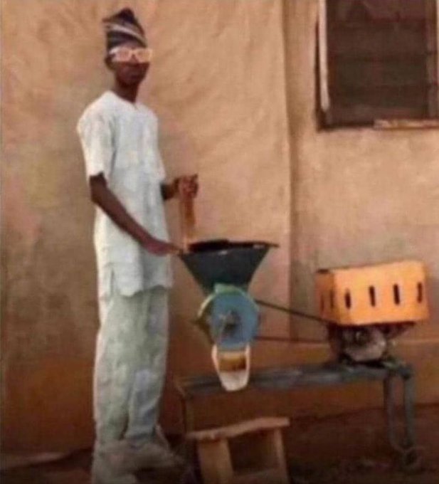A young person in traditional white attire operates a small grinding machine powered by a yellow engine outdoors.