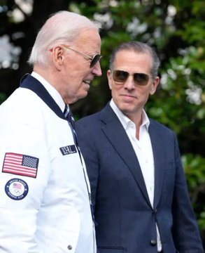 Two men stand outdoors, one wearing a white jacket featuring an American flag patch and a circular emblem, while the other wears a dark suit, sunglasses, and a white shirt with an open collar. The image appears to depict Joe Biden and his son Hunter Biden, whose name is central to the post about the launch of the "$LAPTOP" meme coin referencing the famous laptop incident.