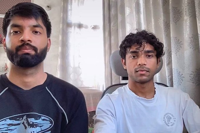Two young men sit side by side in what appears to be a home office setting, with one wearing a black Baltimore Ravens t-shirt and the other in a white shirt, both looking solemnly at the camera. The image likely accompanies the founders of Revalon Finance sharing the difficult news of shutting down their company after exhausting their personal savings, with their somber expressions conveying the heartbreak of the announcement.