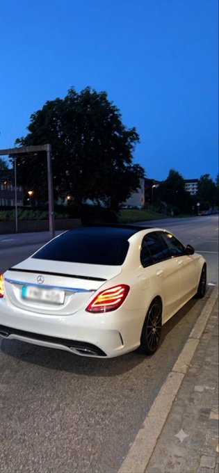 A white Mercedes-Benz sedan parked on a street at dusk under a deep blue sky.