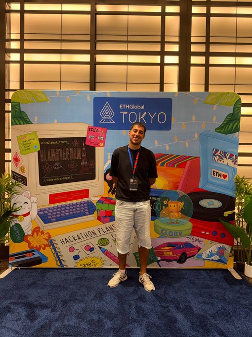 A man standing in front of a colorful ETHGlobal Tokyo event backdrop featuring retro computer, hackathon, and crypto-themed artwork.