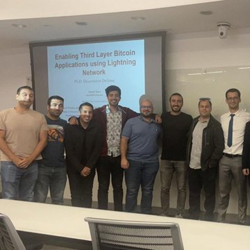 A group of seven men pose together in front of a presentation screen titled 'Enabling Third Layer Bitcoin Applications using Lightning Network' by Dr. Giovanni De Micheli.