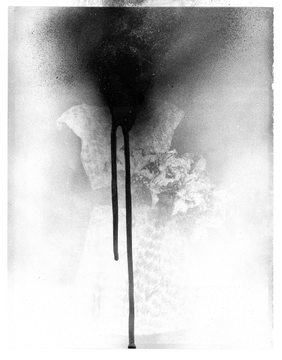 A black and white photograph showing dark liquid (ink or paint) dripping and dispersing in water against a light, cloudy background.
