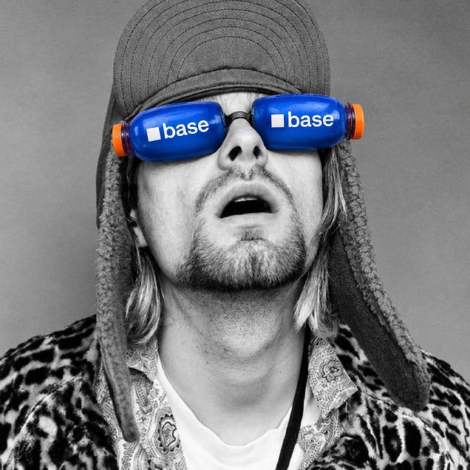 A man in a cap and patterned jacket looking upwards, with two blue "base" branded bottles placed over his eyes in place of glasses.