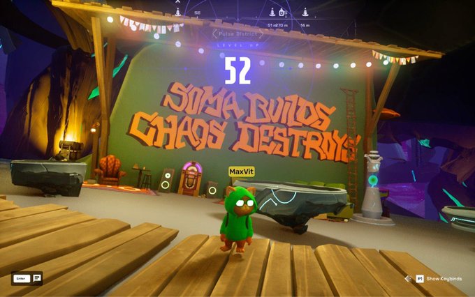 The image shows a cartoon character standing next to a sign that says "Soma Builds Chaos Destroying" with the number 52 on it, possibly indicating a milestone or achievement for the character. The scene also includes a wooden stage set up with various objects such as chairs and a clock, suggesting an event or performance taking place.
