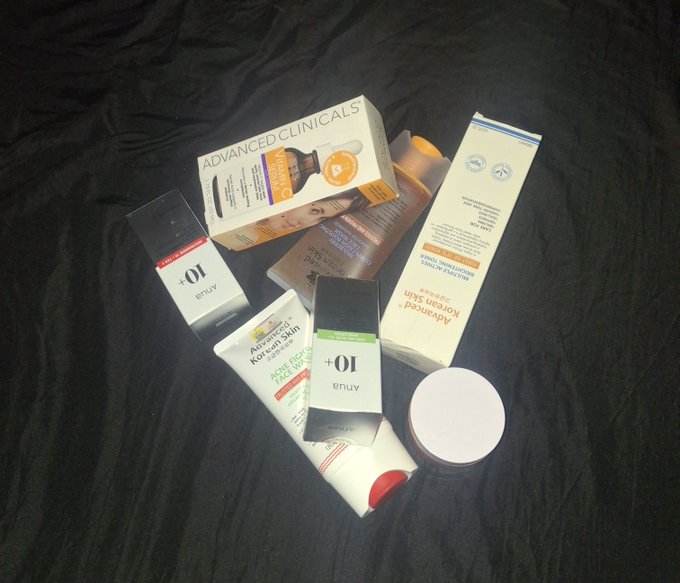 An assortment of skincare products, including brands such as 'Advanced Clinicals', 'Attila', and 'Korean Skin', scattered on a black surface.