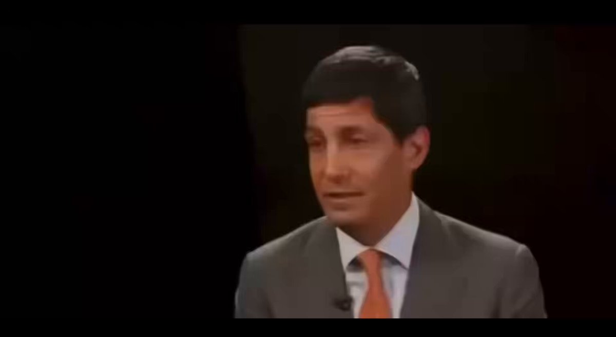 The image features a man dressed in a suit and tie, standing against a black background with an orange tie visible. The man appears to be speaking or giving a presentation, as indicated by his body language and facial expressions. The caption below the image reads "HUGE: Kevin Warsh, the pro-#XRP chairman, leads his first Federal Reserve policy meeting today!".