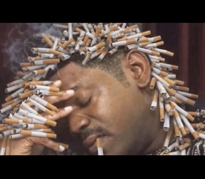 A man with cigarettes stuck all over his hair and face smokes a cigarette, creating a chaotic and surreal image.