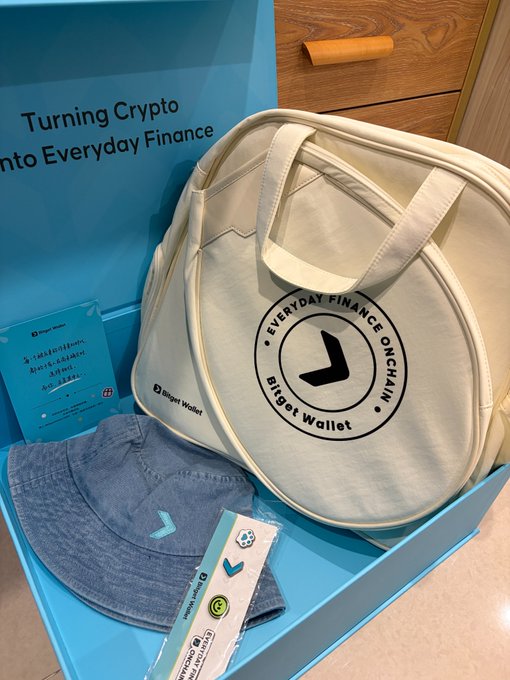 A promotional box for Bitget Wallet, branded "Turning Crypto into Everyday Finance," containing a white circular lunch bag, a denim bucket hat, and stickers.