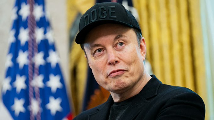 The image features a man wearing a black hat with the word "DOGE" written on it, sitting next to an American flag. The man appears to be looking off into the distance or at something else outside of the frame. The caption provided in the image reads, "Focus on what is in the image and how it relates to the post."