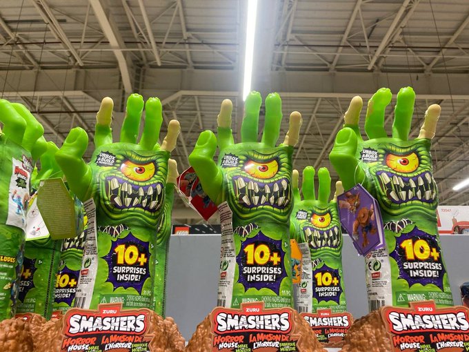 A retail display of "SMASHERS Horror House" toy packages featuring green monster hands with one large eye and sharp teeth, advertising "10+ SURPRISES INSIDE!"
