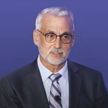A man with gray hair, a beard, and glasses, wearing a dark suit and striped tie, speaks against a blue backdrop during what appears to be a panel discussion or formal address.

The image shows a professional speaker, likely a lawmaker or industry figure, whose remarks align with the post's call for legislative action on crypto regulation through the CLARITY Act.