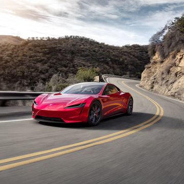 A red Tesla Roadster sports car drives along a winding mountain road, tying into the $TSLA post about the upcoming Tesla Roadster unveiling event and the prediction markets suggesting potential launch-day deliveries.