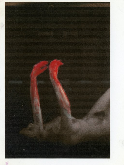 A body lies on its side, with arms extending upwards, hands stained red, suggesting a state of flux.